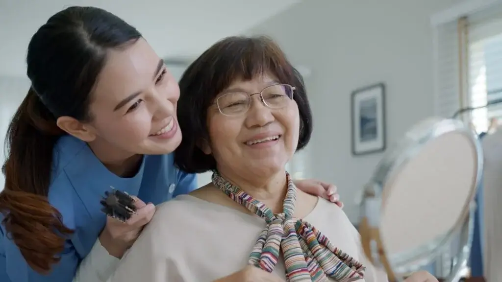 Senior companion care worker helping an elderly woman brush her hair.